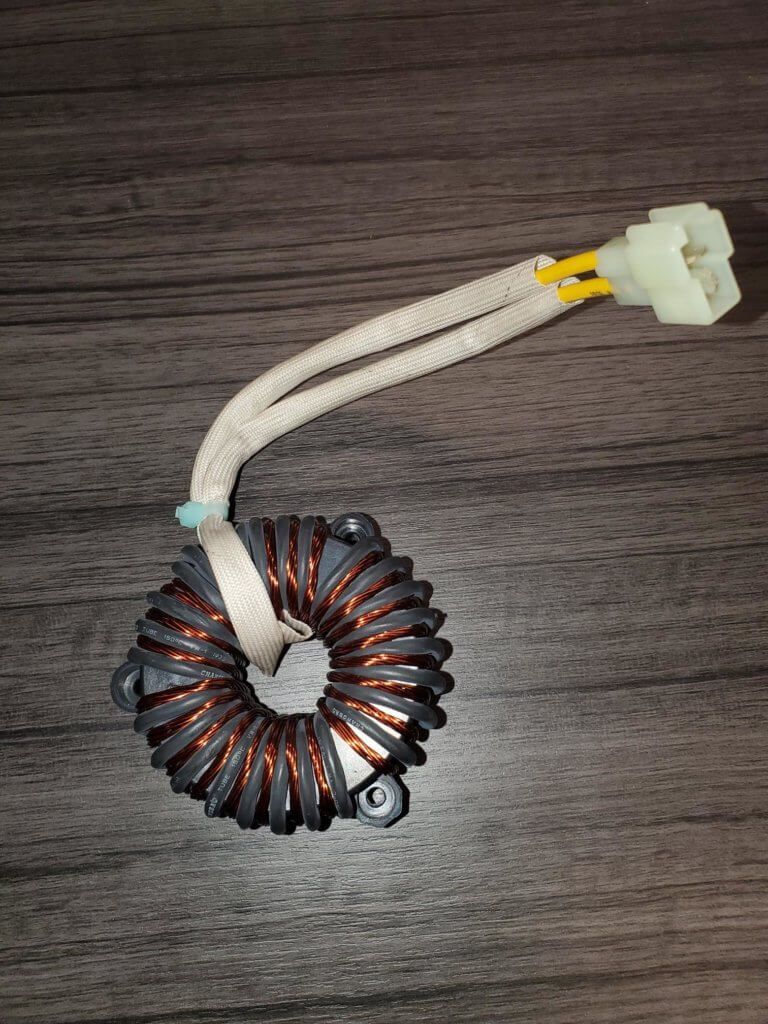 Coiled black toroidal inductor with copper windings and white insulated leads on a wood surface