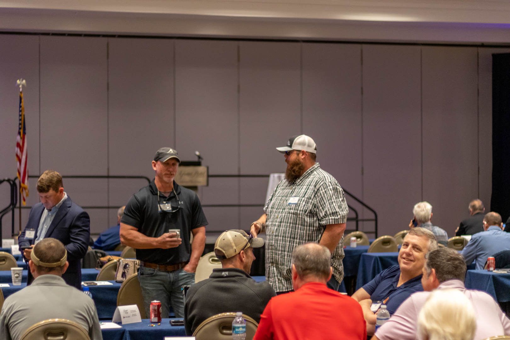 Audience members stand in a conference room, one speaking while others listen.