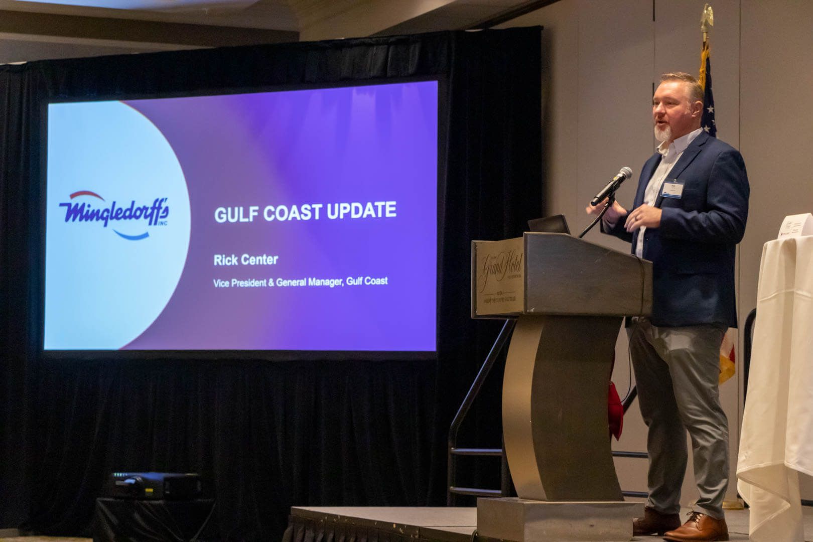 Speaker at podium beside slide titled “Gulf Coast Update” at a conference presentation