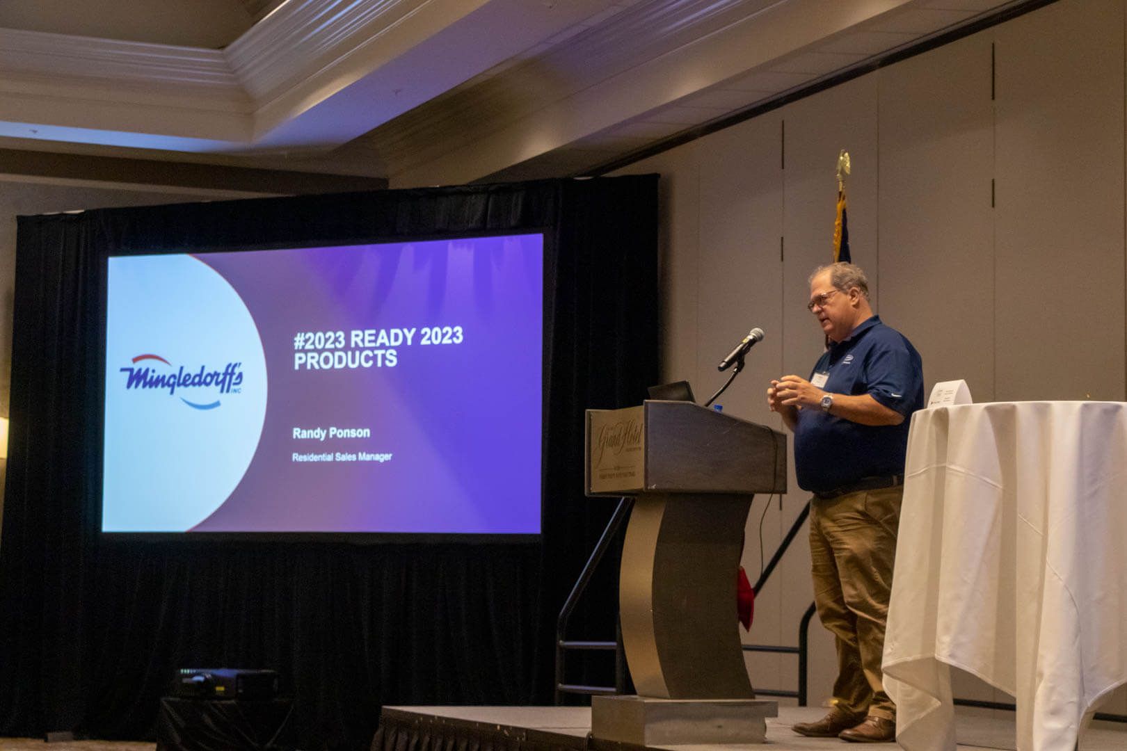 Presenter speaking at a podium beside a slide titled “2023 Product Roadmap” in a conference room.
