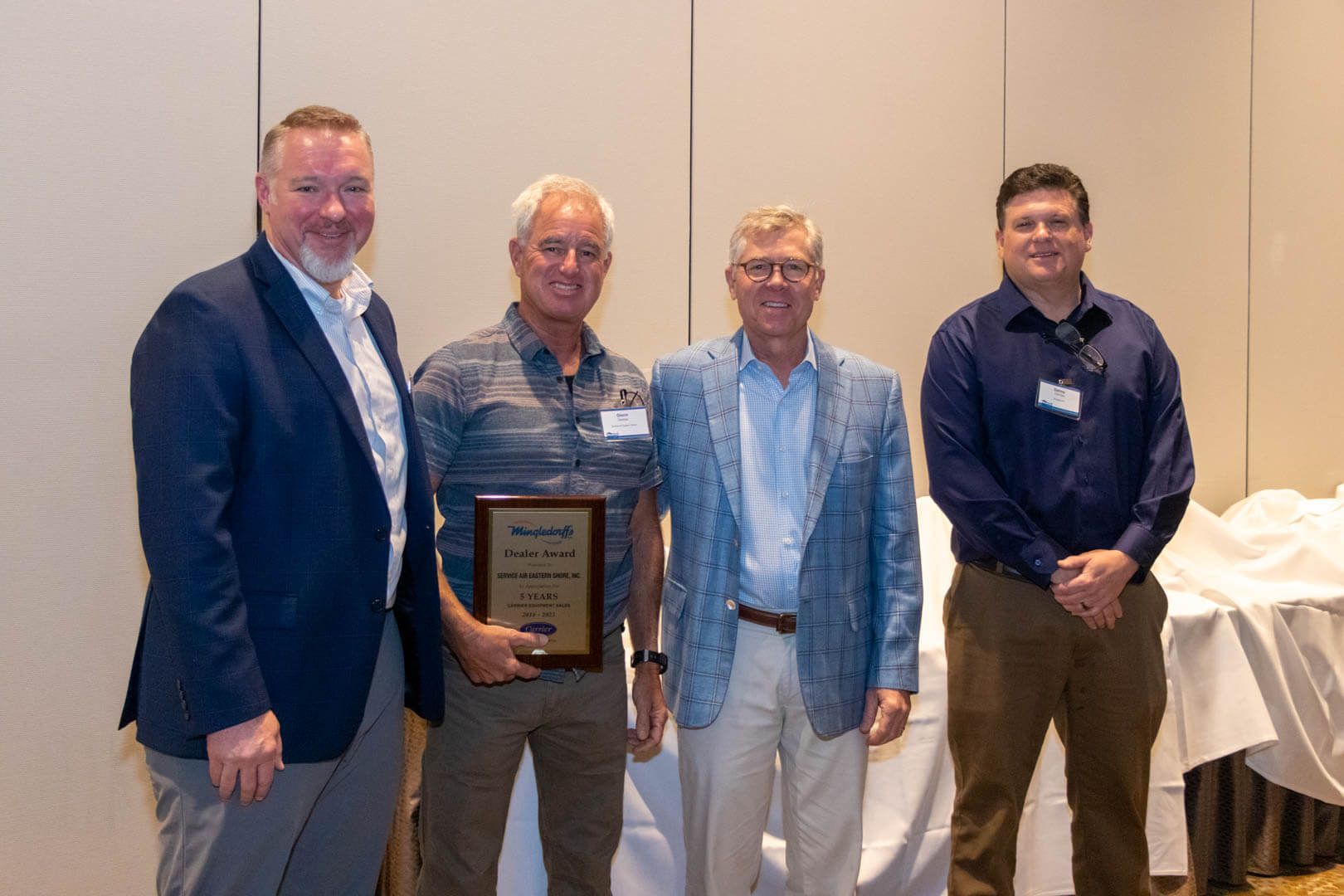 Four men standing indoors, one holding a plaque, at what appears to be an awards event
