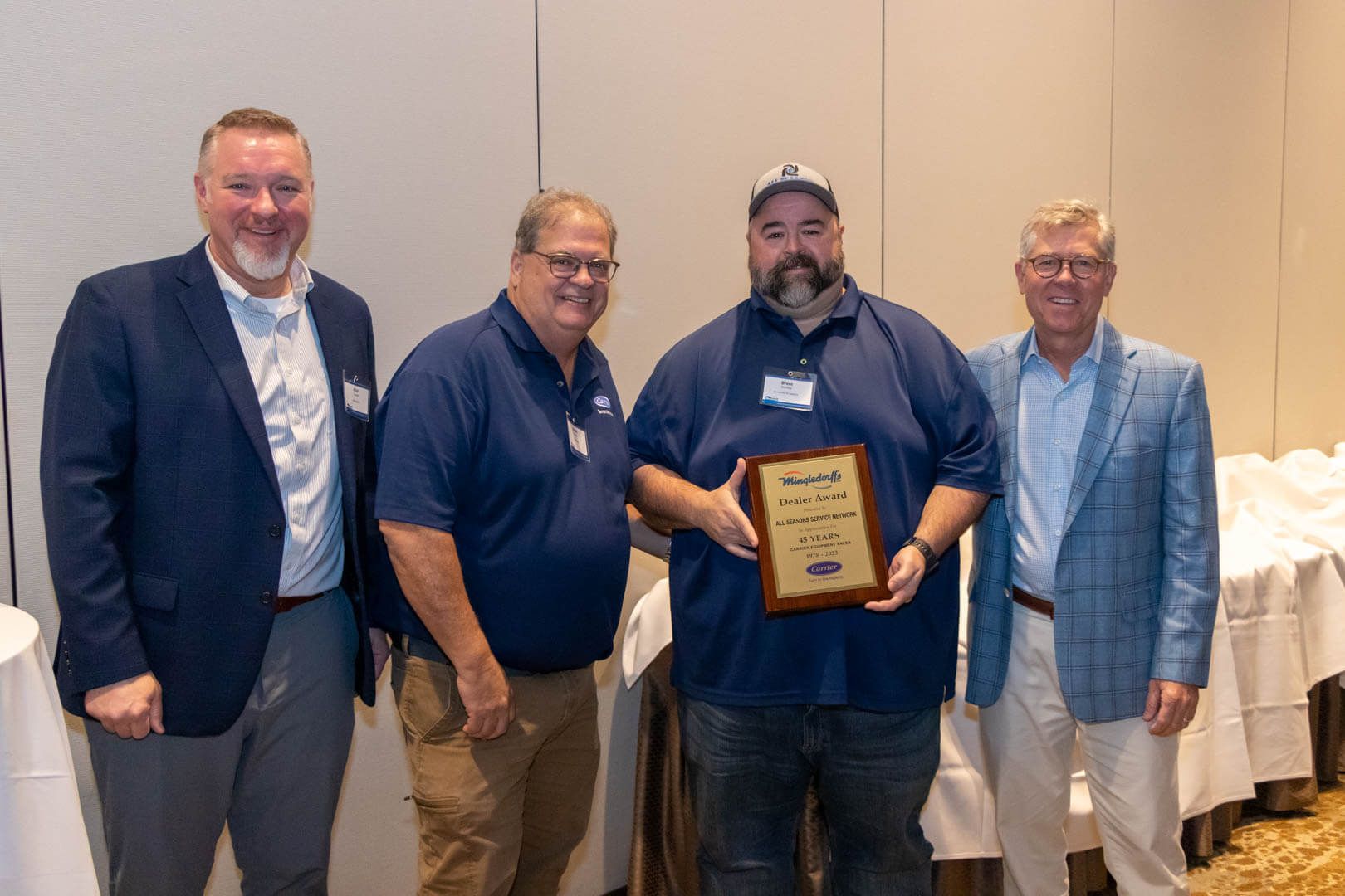 Four men pose at an awards event, one holding a plaque in front of a banquet table.