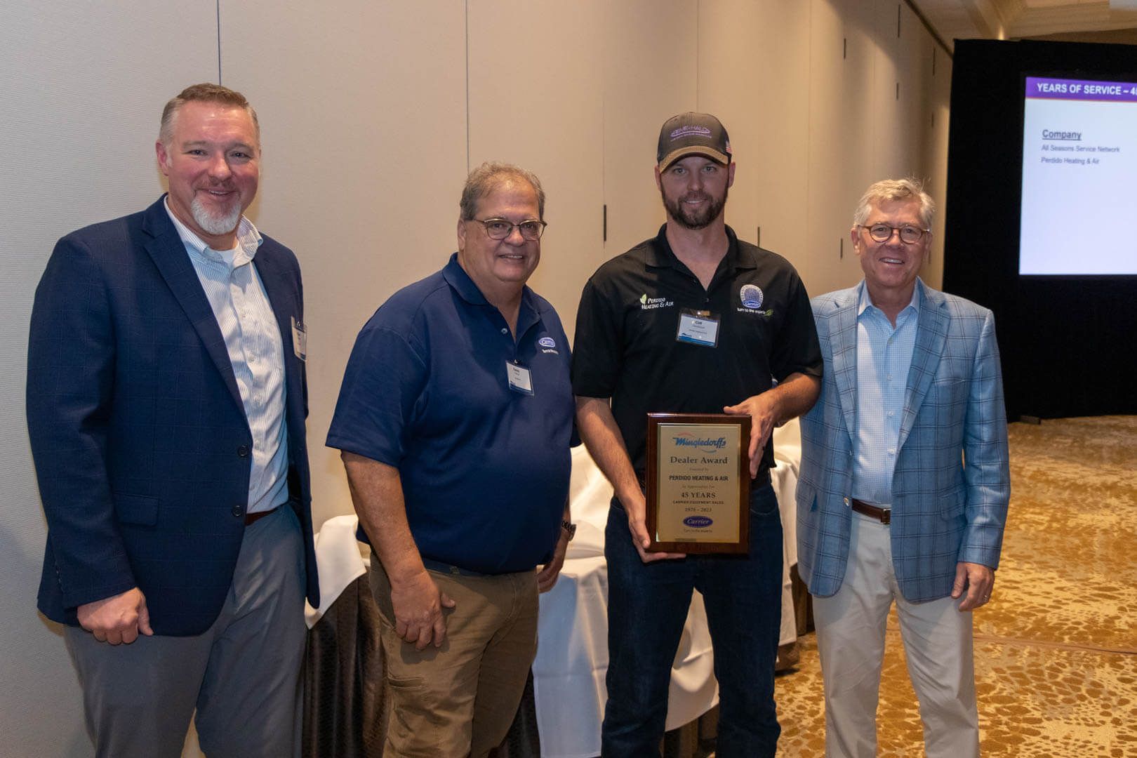 Four men posing indoors with an award plaque at a banquet or conference event.