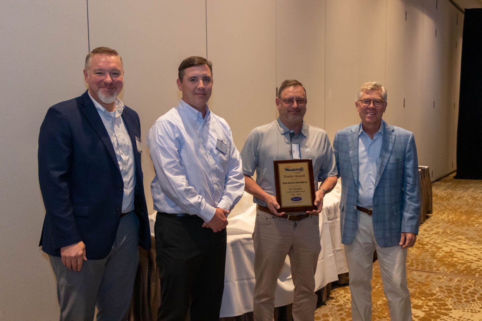 Four men standing indoors, one holding a framed award plaque in a conference room.