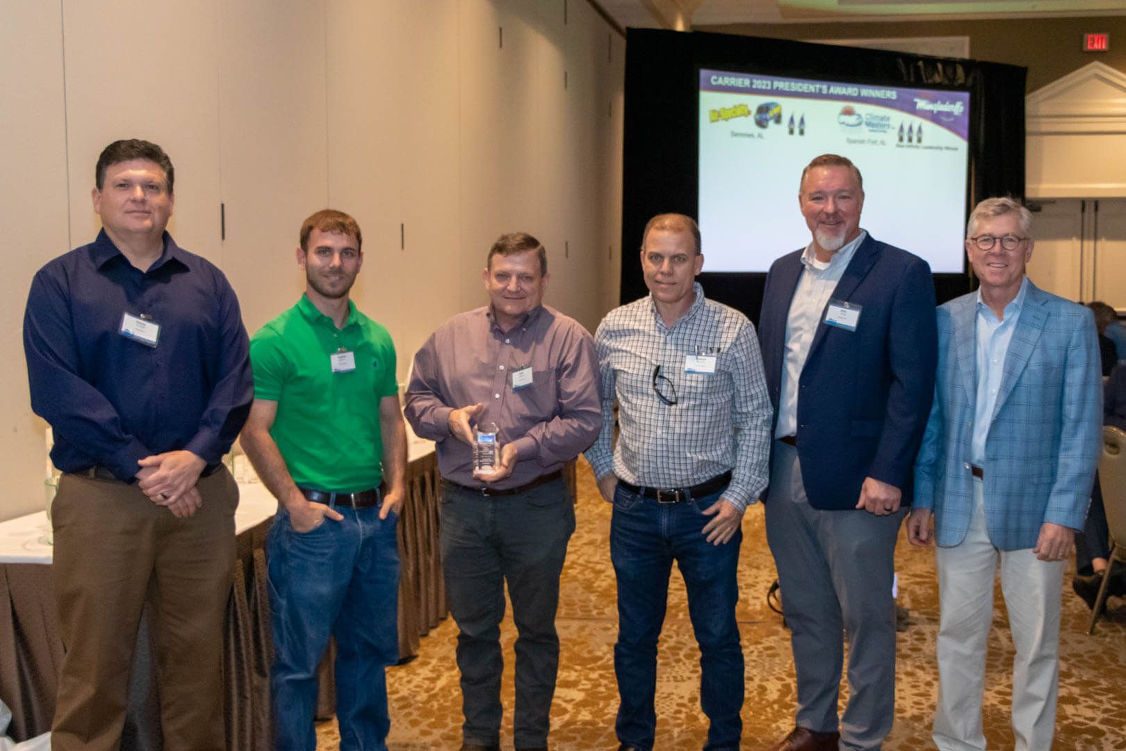 Six men standing in a conference room, posing in front of a presentation screen.