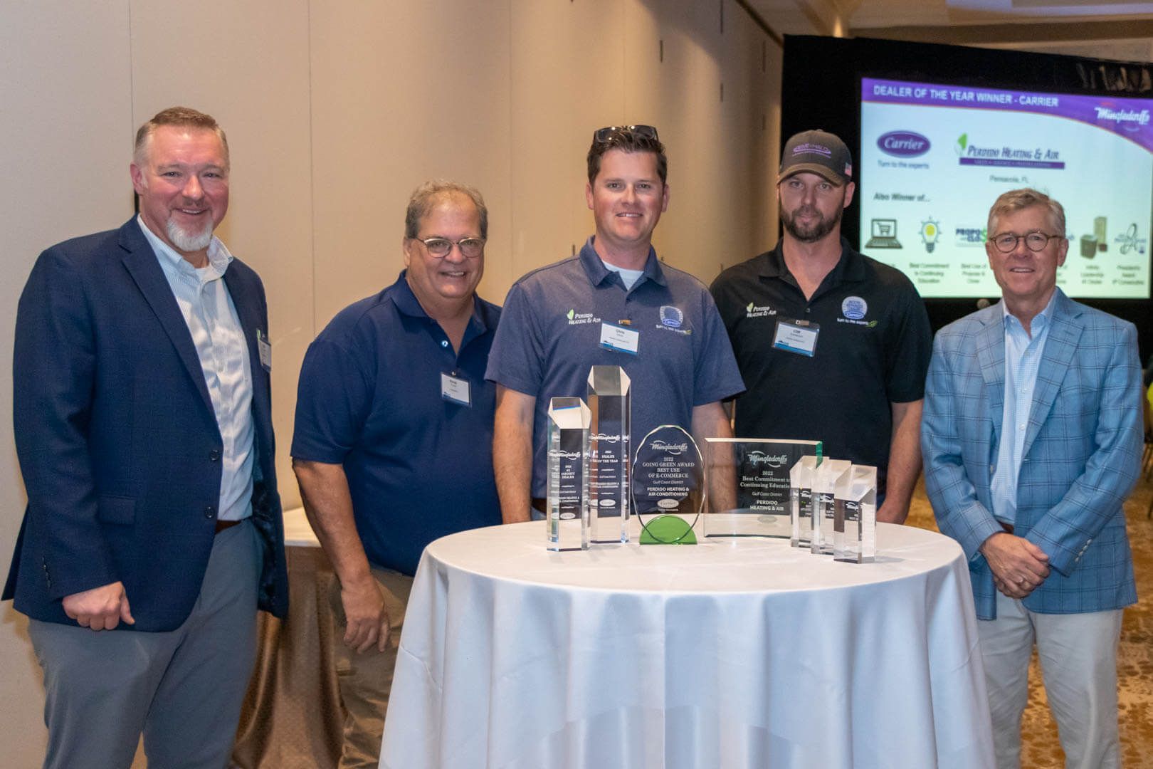 Five men stand behind a table displaying small models at a conference booth.