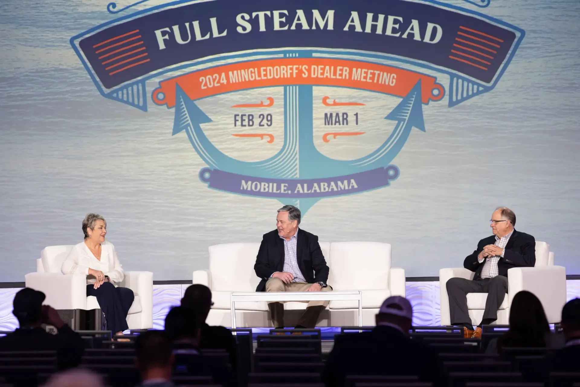 Three speakers seated on stage before a “Full Steam Ahead” conference backdrop.
