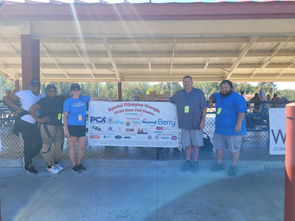 Five people pose in front of a banner under a pavilion at an outdoor event.