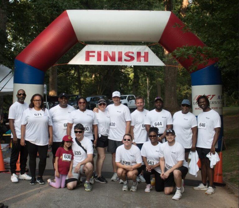 Group of runners posing under a red, white, and blue finish arch at a race event