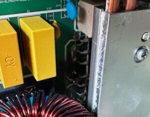 Close-up of a circuit board with yellow capacitors, copper coils, and a metal heatsink.