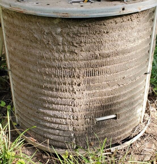 Dirty metal barrel outdoors with a small white pipe protruding near the bottom