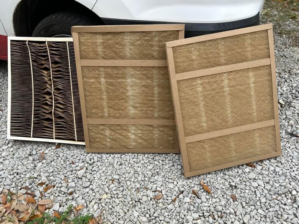 Three outdoor vent covers leaning on gravel, with a white vehicle in the background.