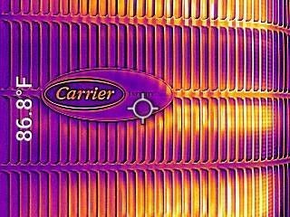 Close-up of a purple Carrier HVAC unit with orange heating fins and a digital temperature reading of 86.8°F