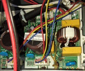 Close-up of tangled wires and electronic circuit boards inside a device, with coils and capacitors visible.