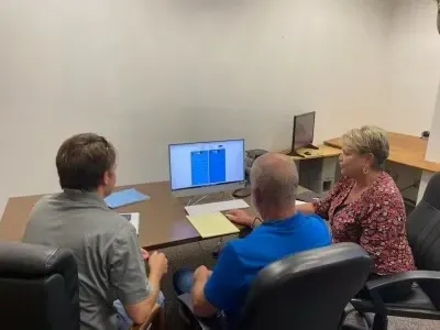 Three people seated at a table, looking at a computer screen in a meeting room.