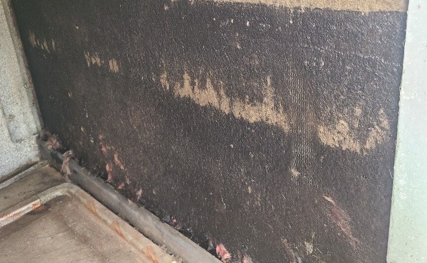 Blackened, soot-covered wall corner with peeling stains and a dusty floor