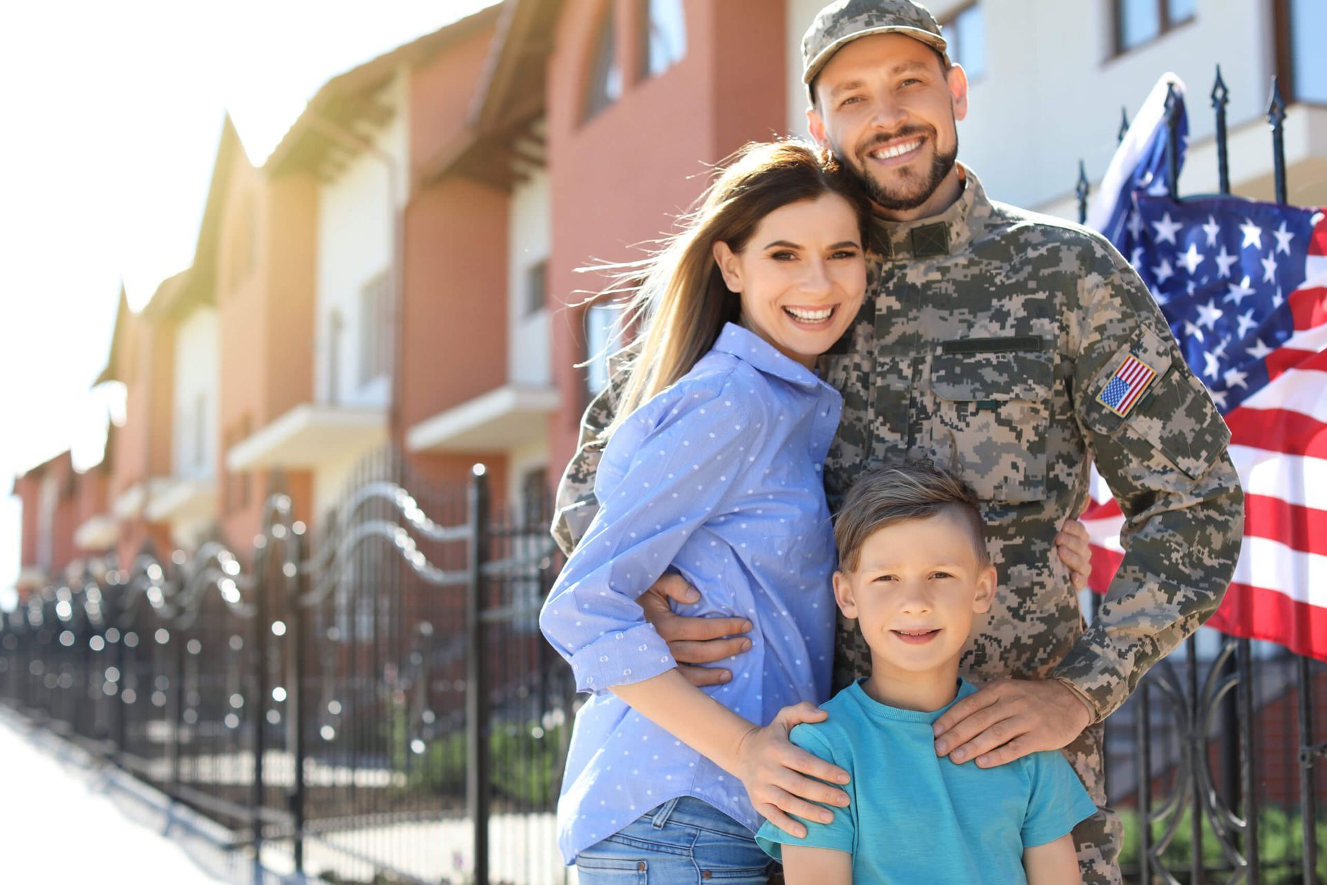Smiling family standing by a fence with an American flag in the background