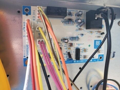 Close-up of a small circuit board with multicolored wires and black cables connected inside a device.