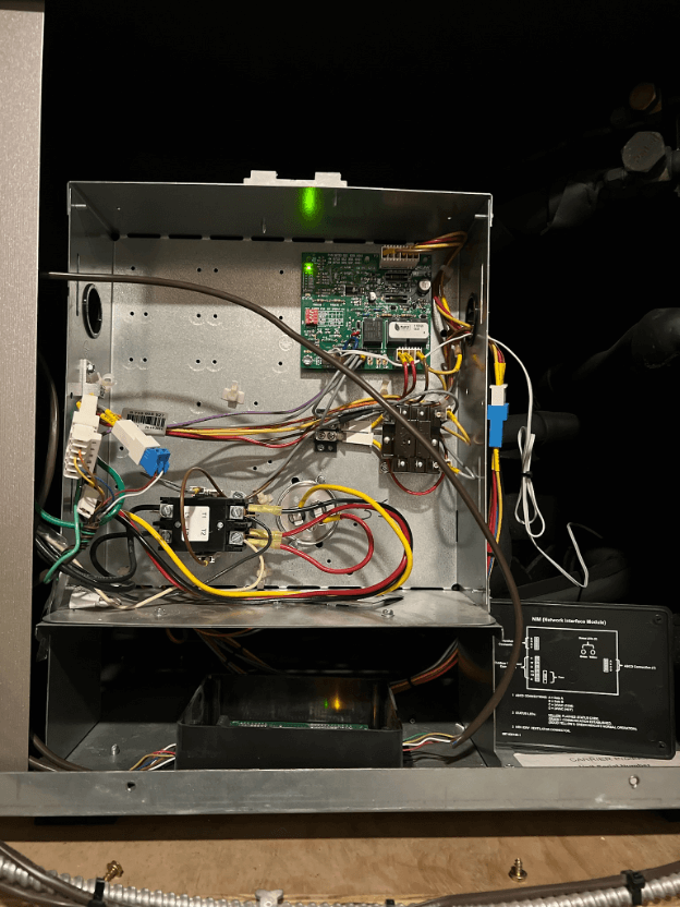 Open metal electronics enclosure with circuit boards, wiring, and a lit green status LED inside.