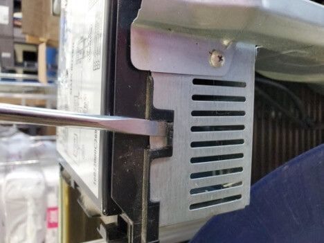 Close-up of a metal screwdriver turning a small screw on a gray vented appliance panel