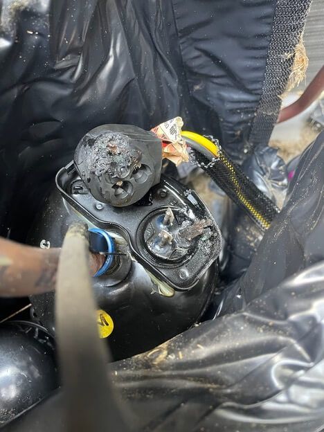 Black scuba or dive gear with a damaged, melted-looking regulator and hoses in a wet setting