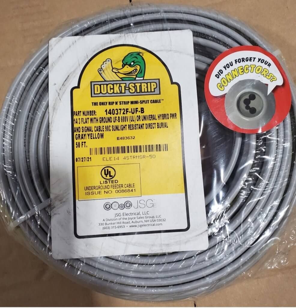 Coiled gray steel cable with yellow product label and red spool tag on a cardboard surface