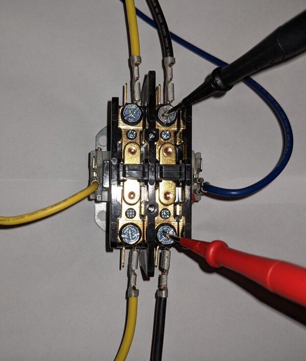 Close-up of an electrical relay with yellow, blue, and red wires attached to its terminals.