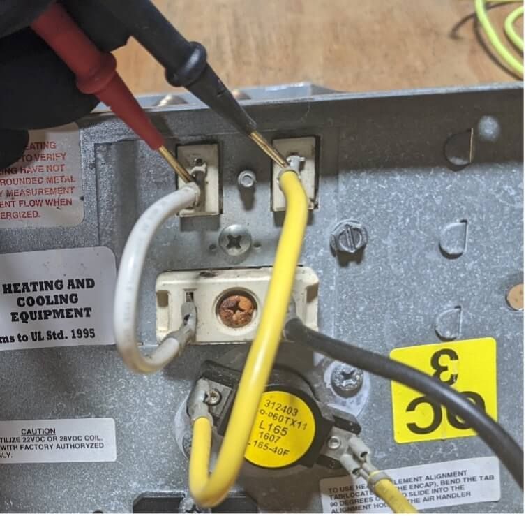 Close-up of HVAC wiring terminals with red, black, and yellow wires being connected.