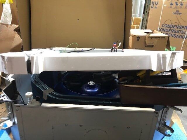 Damaged white appliance with a blue circular component inside a cluttered storage area