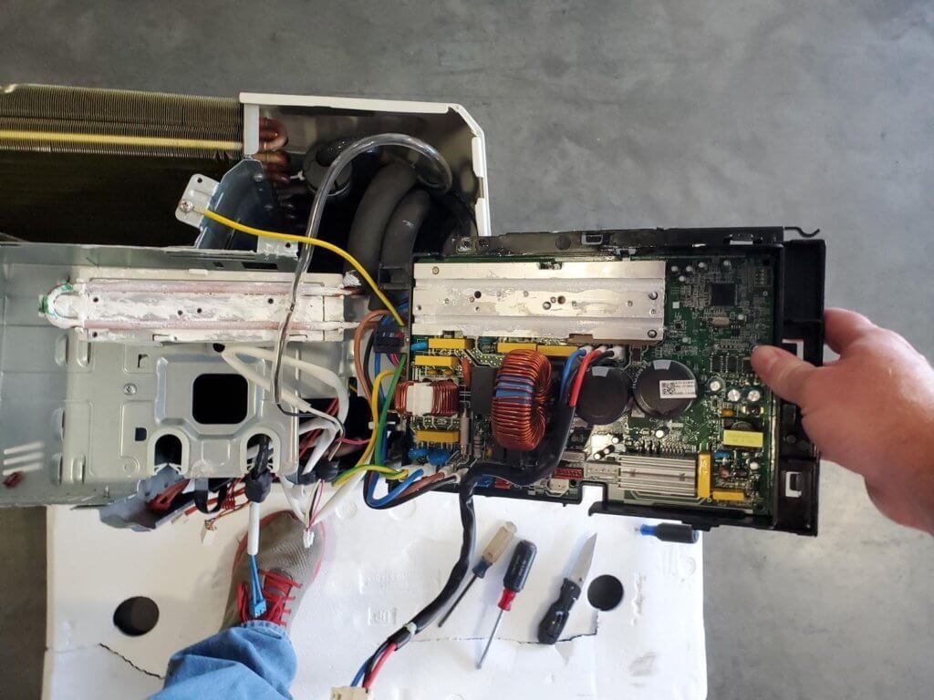 Person holding an open electronic device with exposed circuit board, wires, and metal chassis.