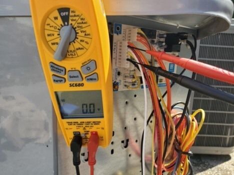 Yellow digital multimeter clipped to wires inside an open electrical panel