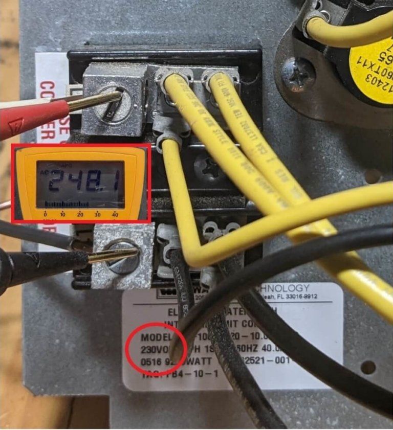 Close-up of electrical panel wiring with a handheld multimeter reading 242.
