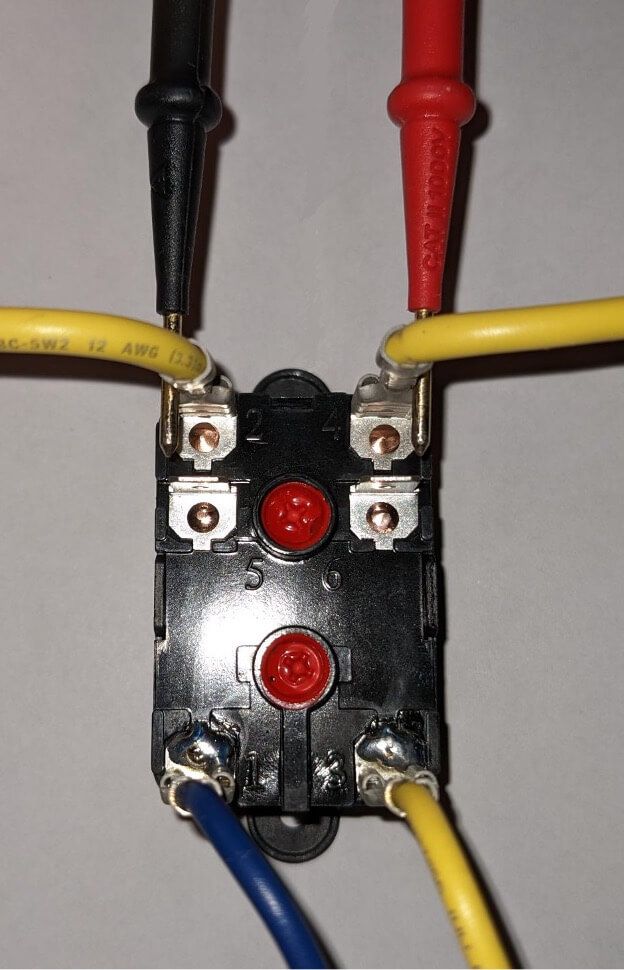 Close-up of a black electrical component with red buttons and connected red, yellow, black, and blue wires.