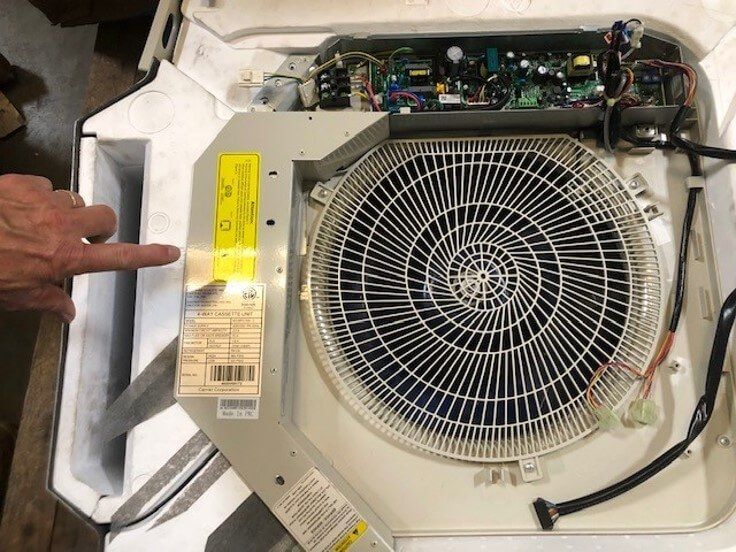 Open appliance with large fan assembly and circuit board, a hand pointing at a label.