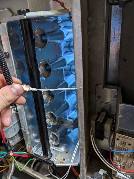 Hand holding a test probe inside an open electrical control panel with blue wiring and components