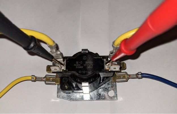 Close-up of a black thermostat switch with red, yellow, blue, and black wires clipped to its terminals.