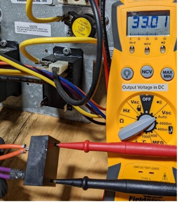 Digital multimeter probing wires in an electrical panel, displaying 331 on a yellow device.