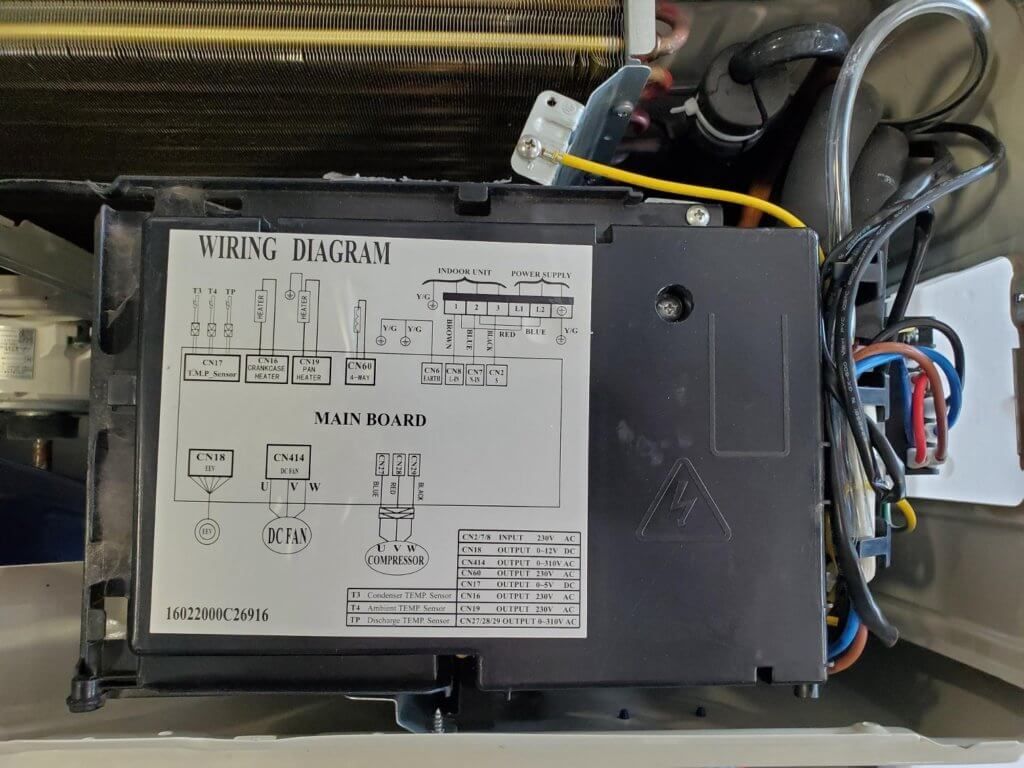 Close-up of a black electrical control box with wiring and a labeled diagram inside a machine compartment