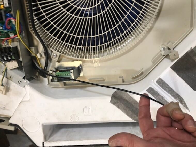 Inside an appliance, a hand points to wiring and a small circuit board near a fan