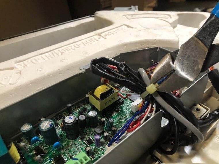 Electronics board with capacitors and wires, clamped by pliers inside a white plastic case
