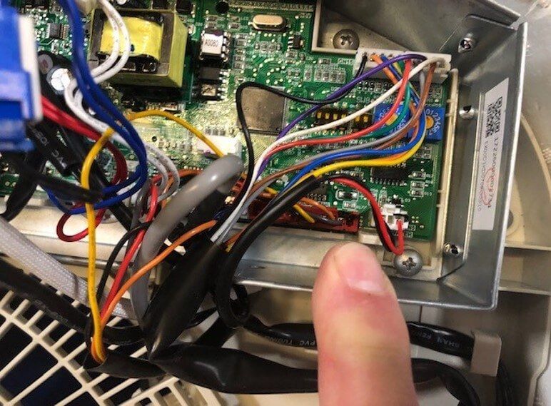 Close-up of a device’s circuit board with multicolored wires and a finger pointing at a connector