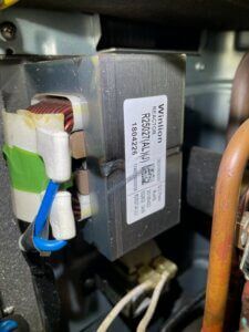 Close-up of an electrical transformer with white wires and blue tie inside a metal appliance.