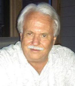 Smiling man with white hair and mustache wearing a white shirt indoors