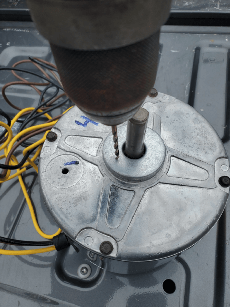 Close-up of a drill pressing into a metal circular plate with wires on a workbench