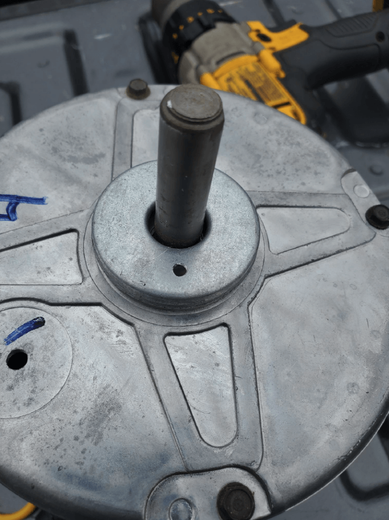 Close-up of a gray metal circular tool head with a vertical shaft, on a workbench near a drill.