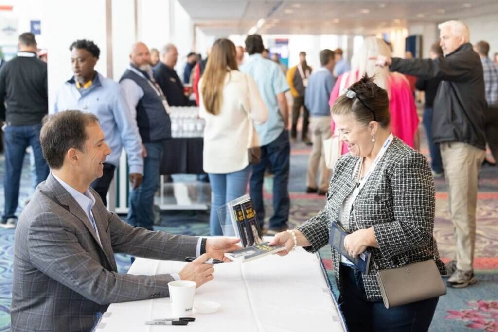 People chatting at a conference reception table in a bright lobby.