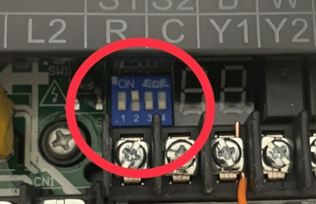 Close-up of a blue DIP switch on an electrical terminal block, circled in red.