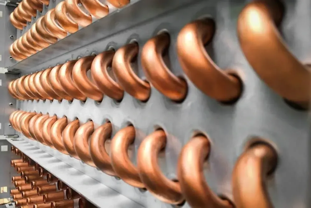 Rows of shiny copper pipes or coils mounted on a gray industrial panel, viewed at an angle.