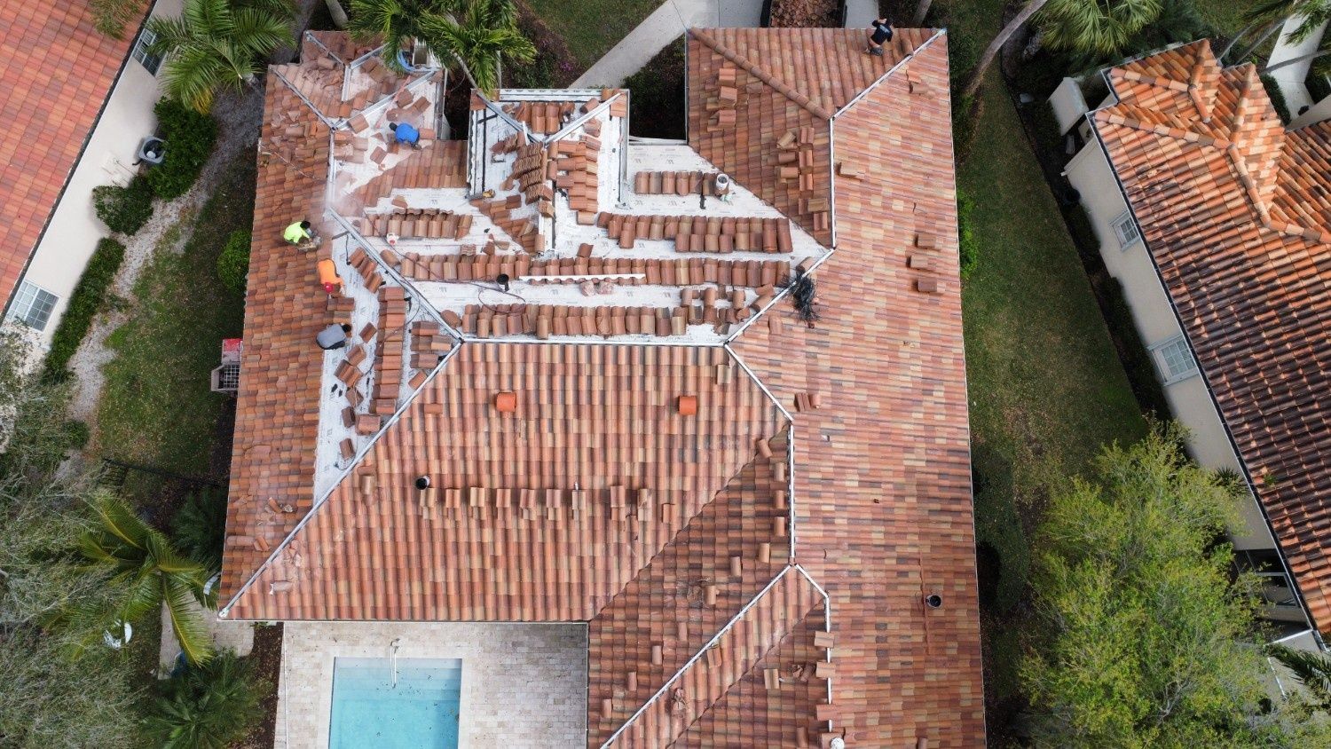 Aerial view of a red-tiled roof with weathered white debris and a small turquoise pool below.