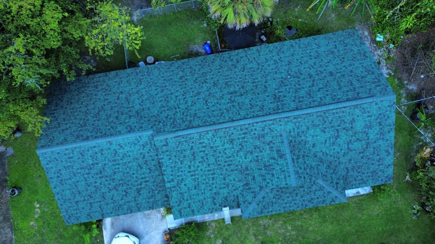 Aerial view of a house with a blue roof surrounded by green trees and lawn.
